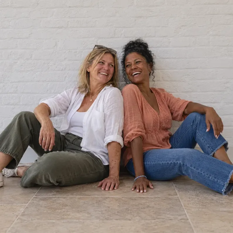 Anna and Monique, the hosts of Art Therapy, sitting back to back and laughing